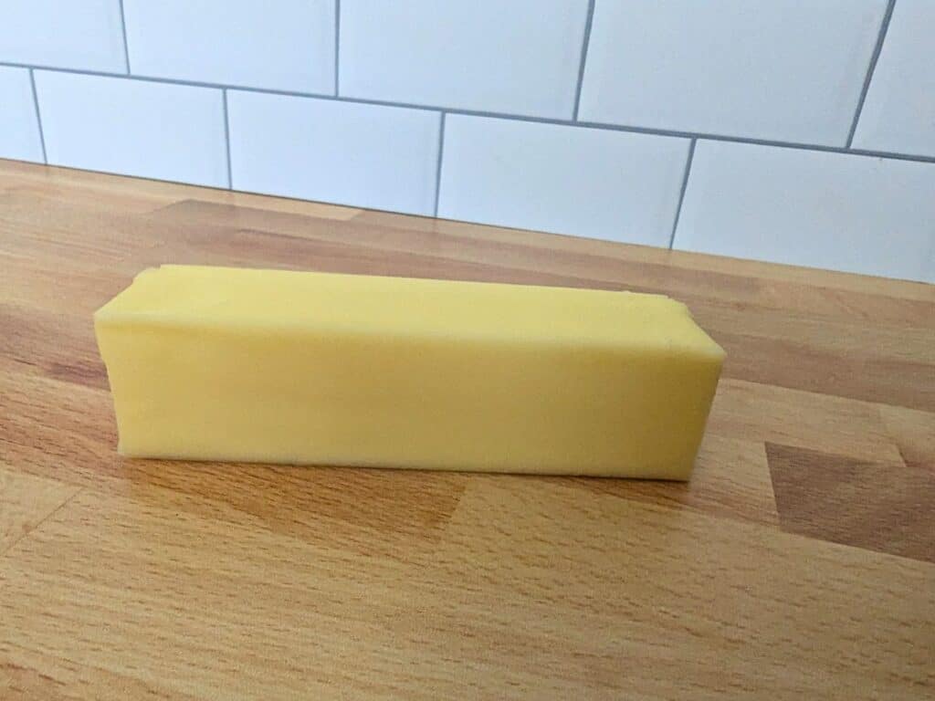 Image shows a Close up of a stick of butter on a wooden table.