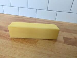 Image shows a Close up of a stick of butter on a wooden table.