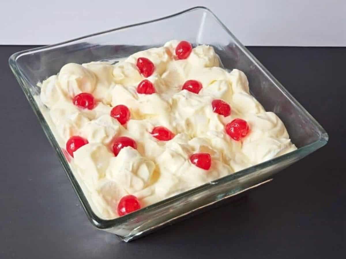 Bowl of marguerite salad topped with cherries on a black counter.