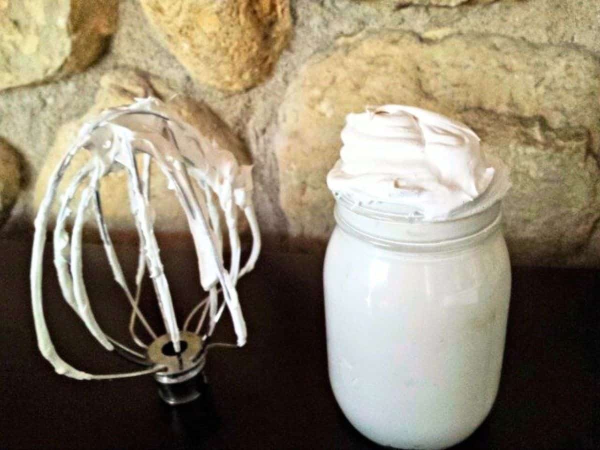 Image shows Stiff peaks of homemade marshmallow fluff being lifted from a glass bowl.