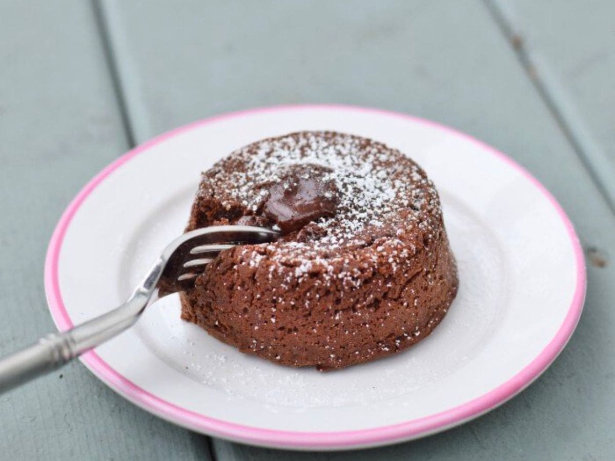 Image shows a fork pulling a bite from a molten chocolate cake on a white plate.