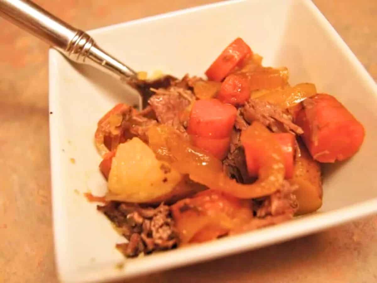 A plate of sliced roast meat topped with gravy, sautéed onions, and a few diced tomatoes, accompanied by a serving of mashed potatoes.