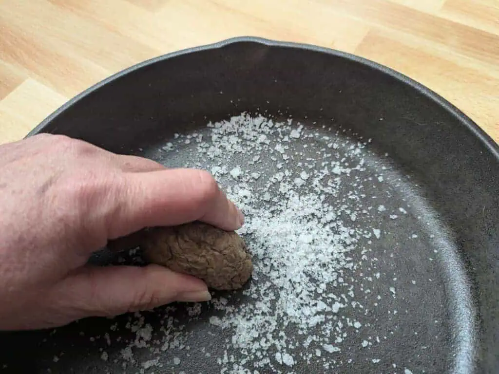 Image shows a Hand rubbing a potato and salt into a cast iron pan to clean it.