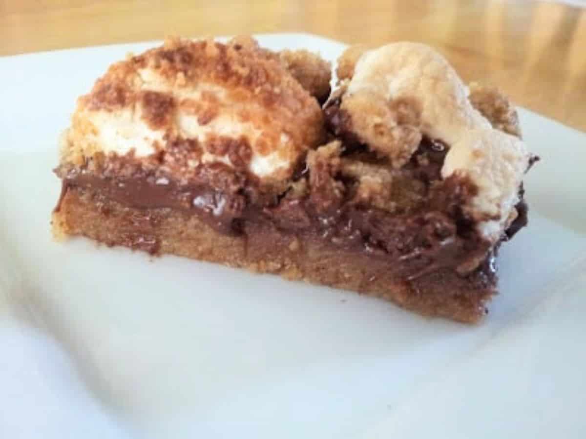 Image show a closeup of a Chewy Smores bar on a white plate.