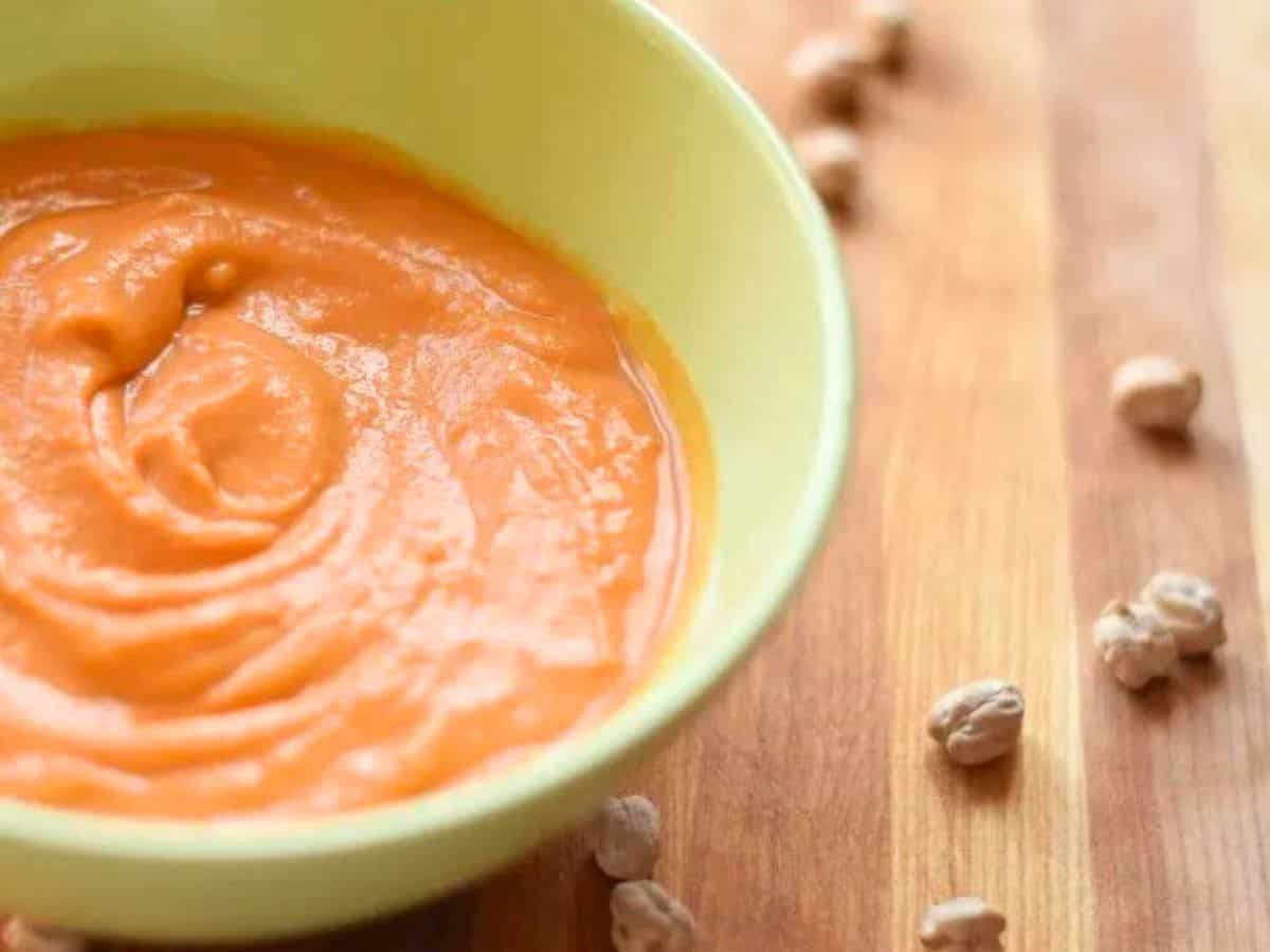 Image shows A bowl of creamy chickpea tomato soup with dried chickpeas around it.