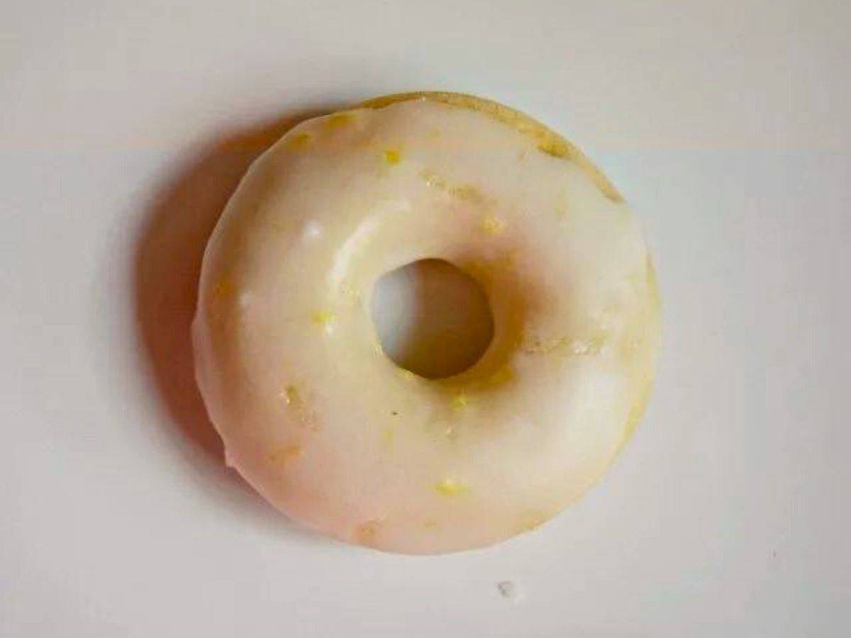 Image shows Baked lemon mini donuts held over more on a wire rack.