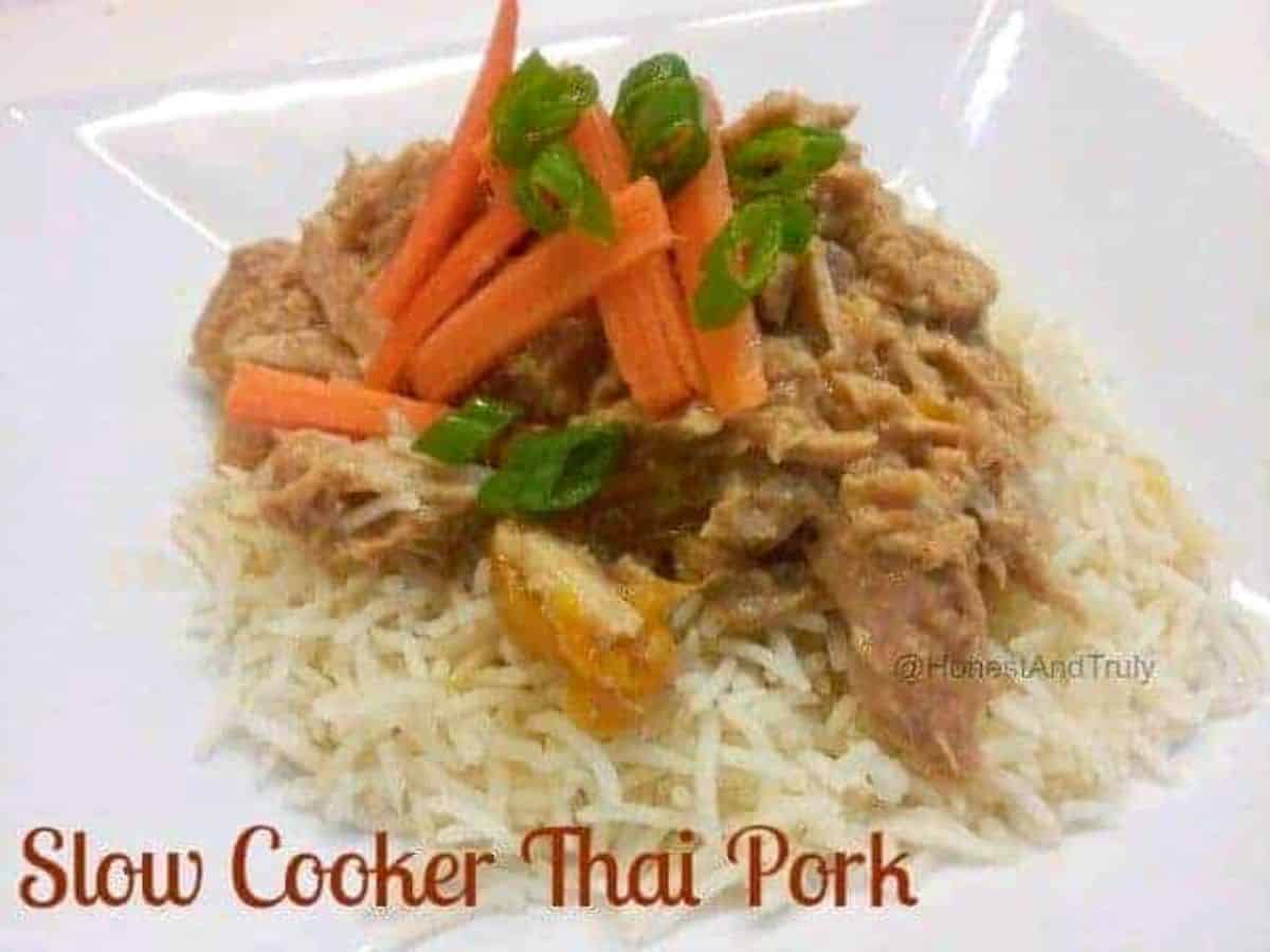 Image shows Slow Cooker Thai Pork on a bed of rice on a white plate with sliced carrots and green onion on top of it.