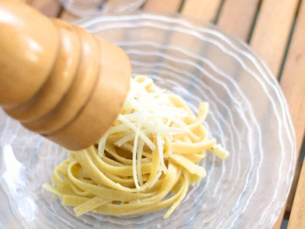 Image shows adding fresh ground pepper to delicious cacio e pepe.