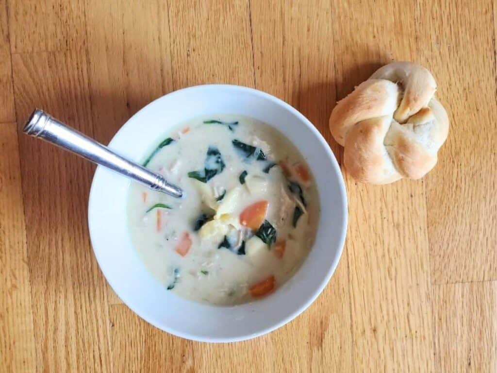 Image shows bowl of creamy tortellini soup with a dinner roll.