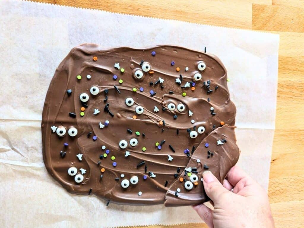 Image shows a hand Breaking Halloween bark into pieces.