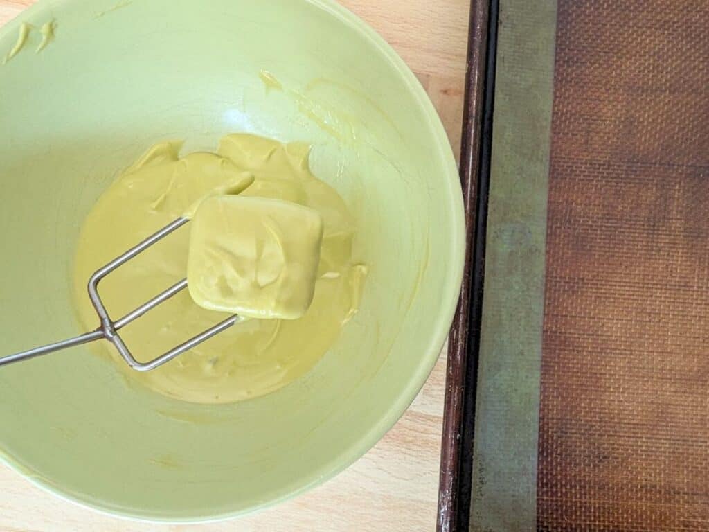 Image shows Dipping a pretzel into green chocolate with a tool.