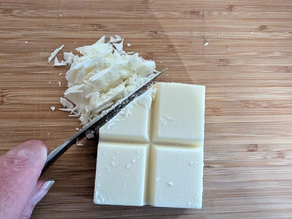 Image shows a Half chopped block of almond bard on a wooden cutting board.
