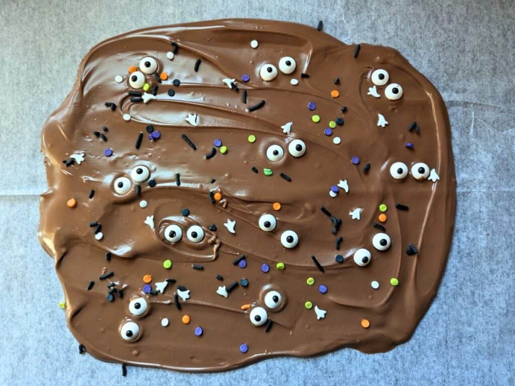 Image shows Halloween Chocolate bark still melted with items pressed in and waiting to dry on parchment paper.