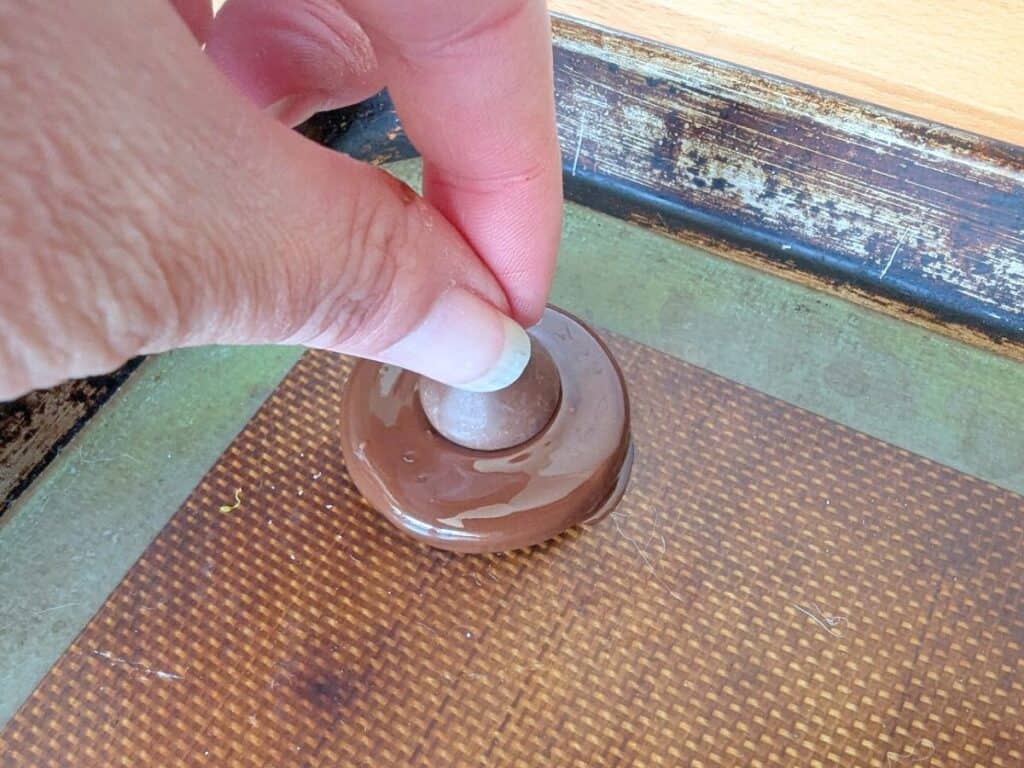 Image shows a hand Placing kiss on a chocolate dipped oreo.