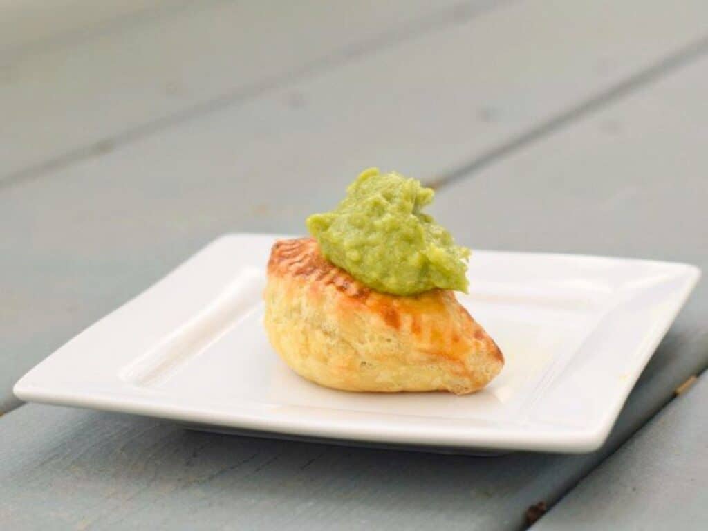 Image shows easy to make puff pastry beef empanada on a plate with guacamole on top.