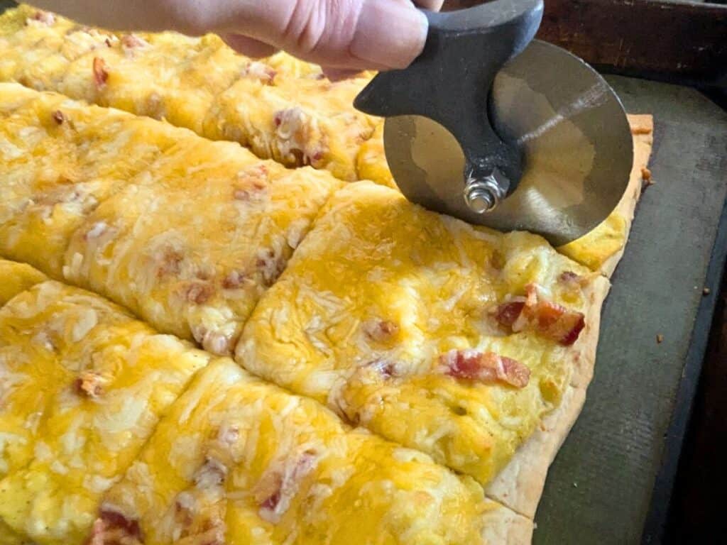 Image shows breakfast pizza cut using pizza wheel.