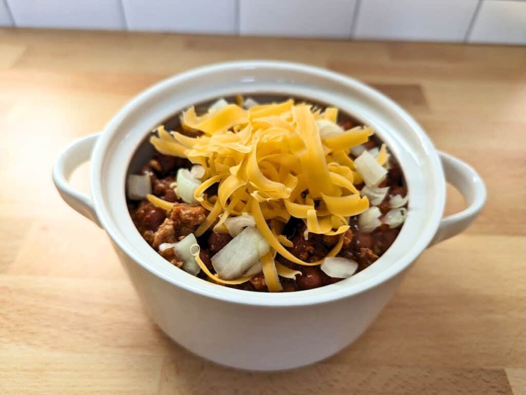 Image shows slow cooker pork chili served in a serving pot with toppings.