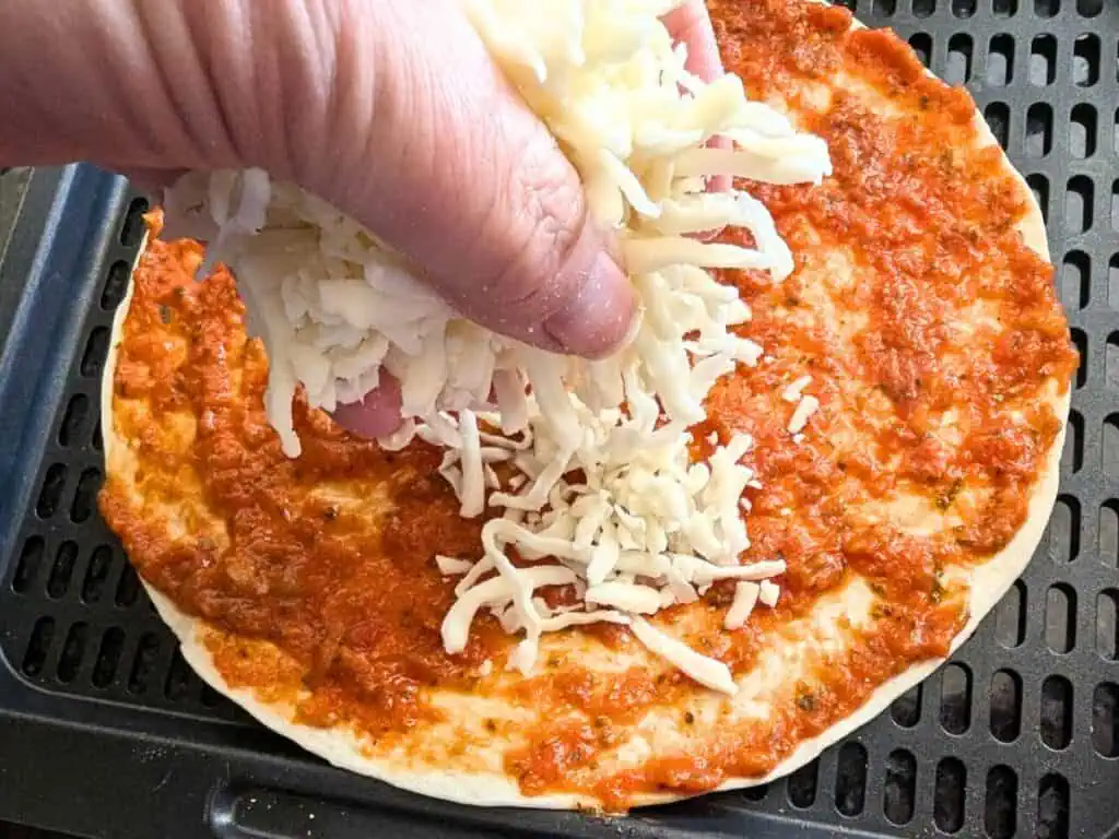 Image shows adding mozzarella cheese on top of the tomato sauce.