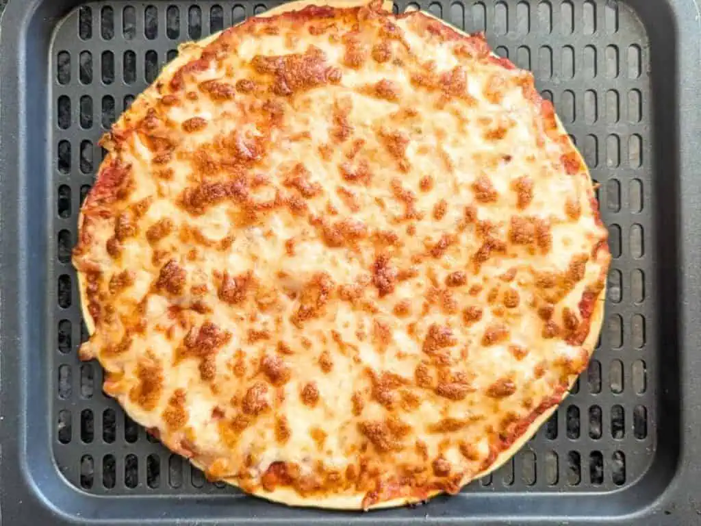 Image shows cooked tortilla pizza on an air fryer tray.