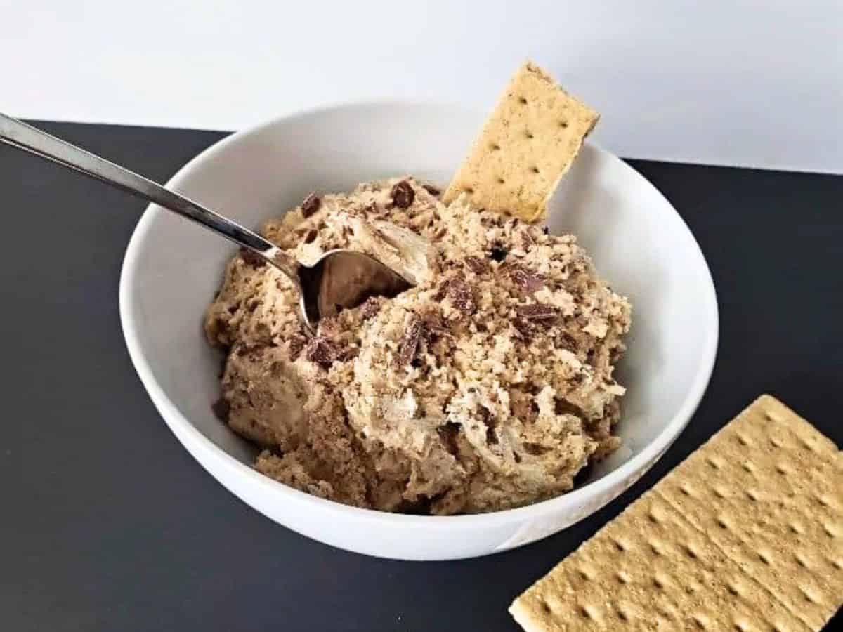 Photo shows a white bowl filled with edible chocolate chip cookie dough and graham crackers around it.