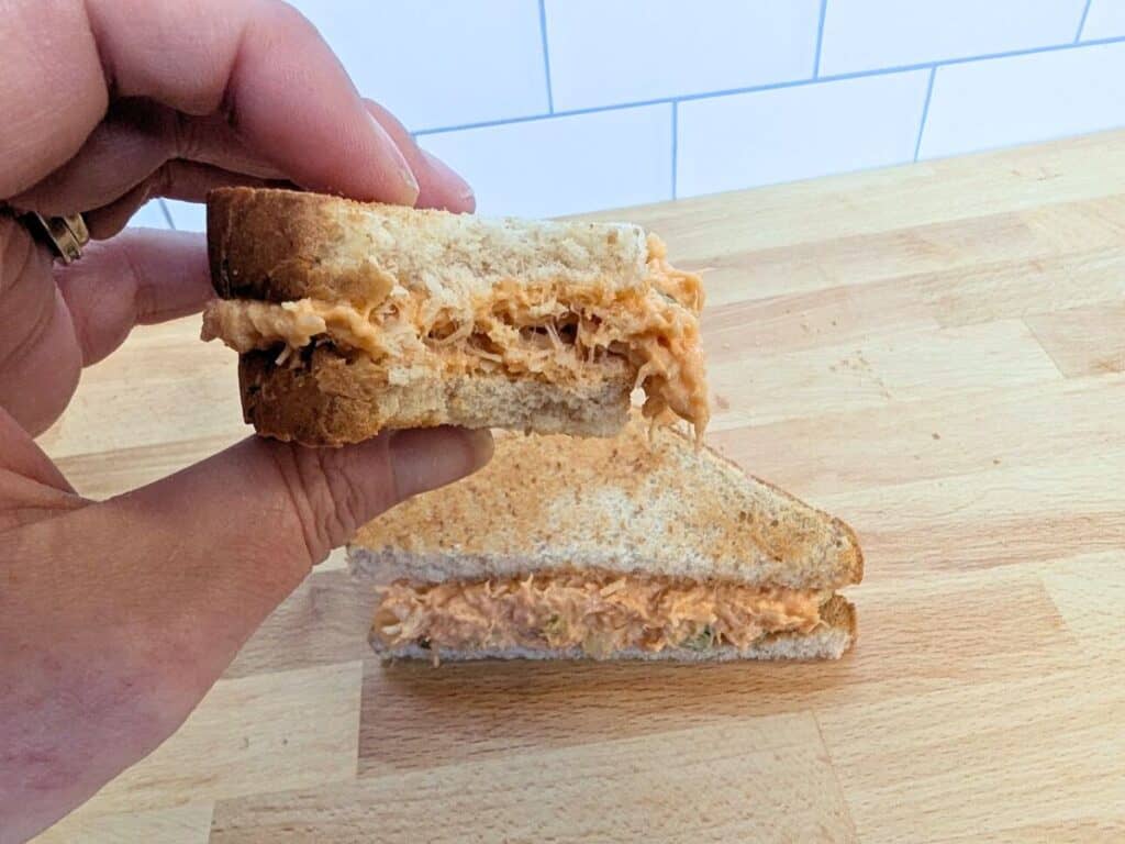 Image shows a hand holding a buffalo chicken salad sandwich.