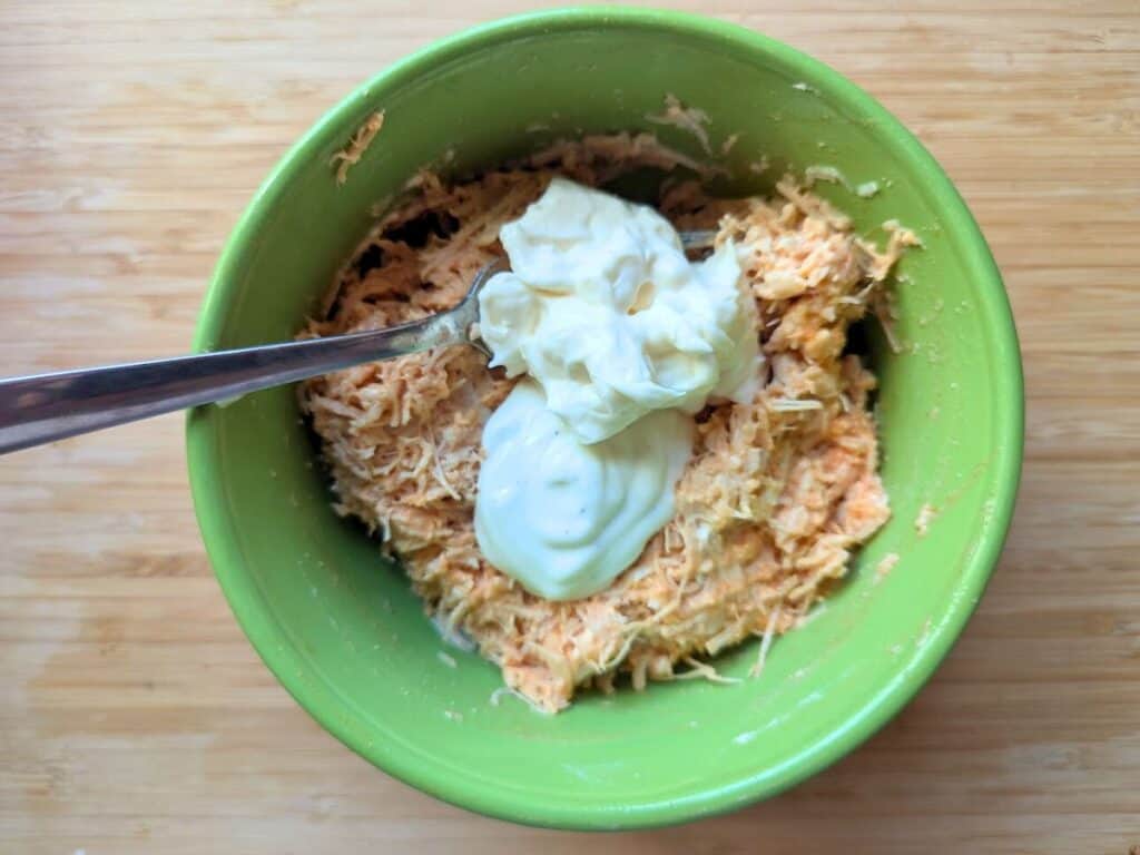 Image shows adding mayonnaise to nearly finished buffalo chicken salad in a bowl.