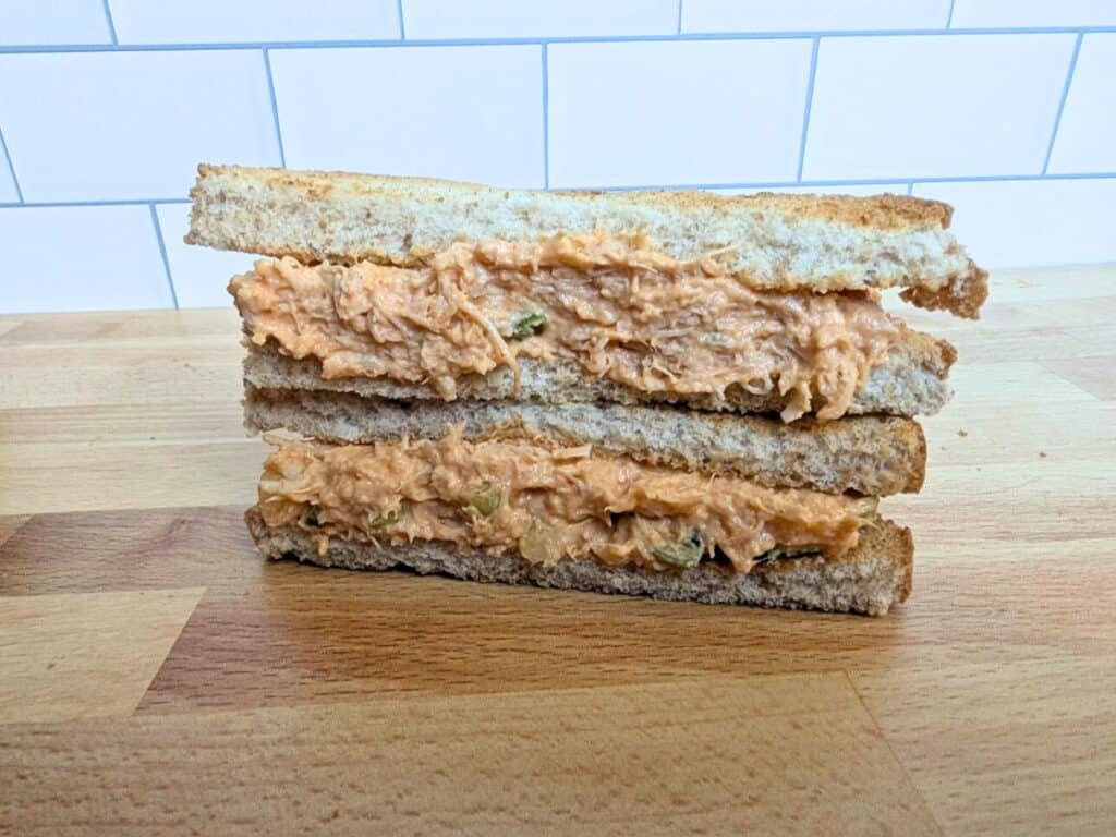 Image shows buffalo chicken salad sandwich on a wooden platform.