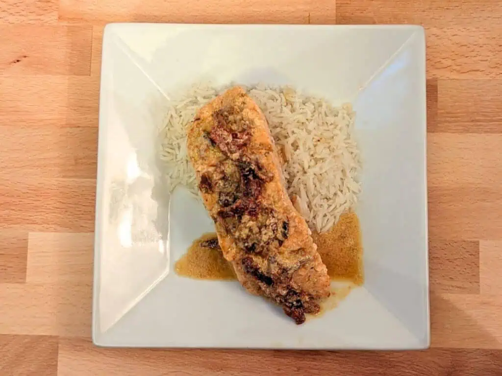 Image shows easy to make creamy sun-dried tomato salmon on top of rice.
