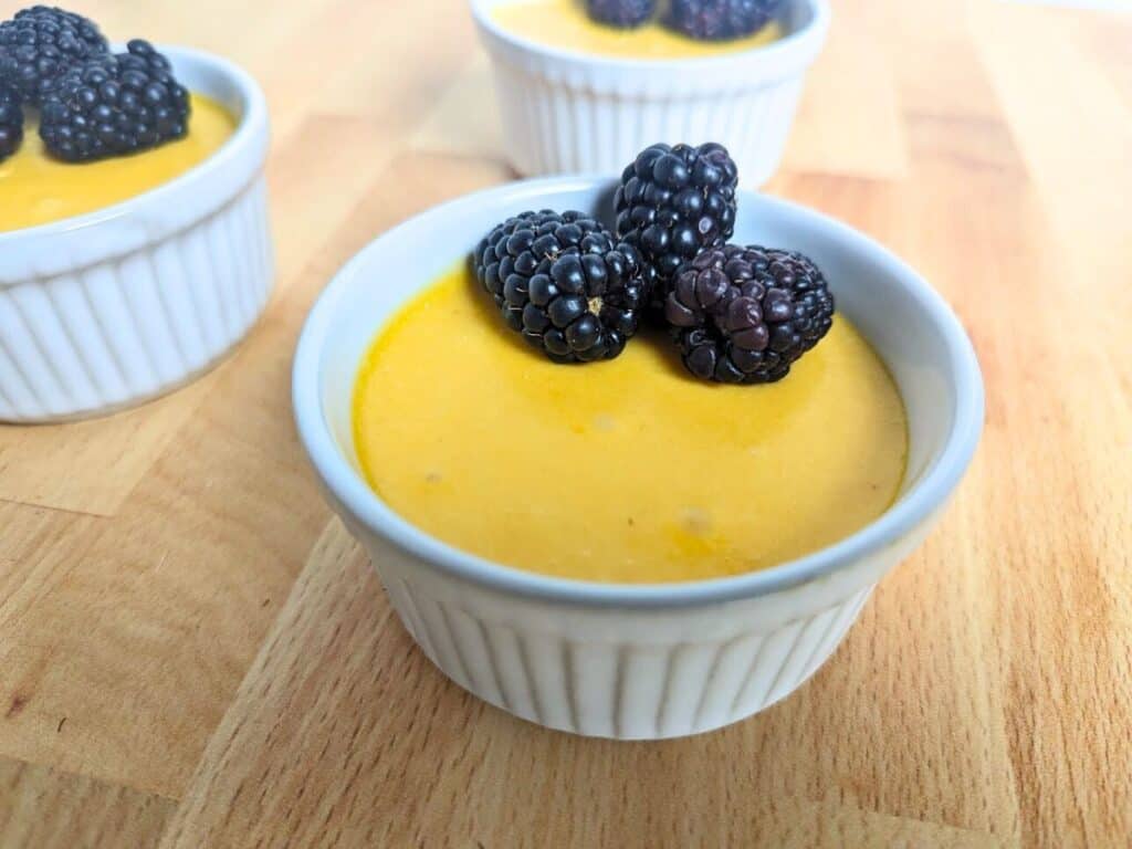 Image shows mango mousse in a ramekin with blackberries on top.
