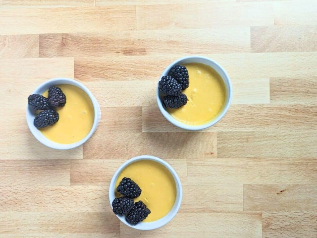 Image shows three ramekins of mango mousse on a wooden board.