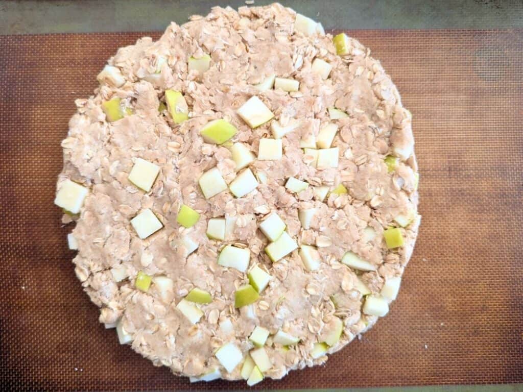 Image shows Apple scone dough shaped into a round on a Silpat baking mat.