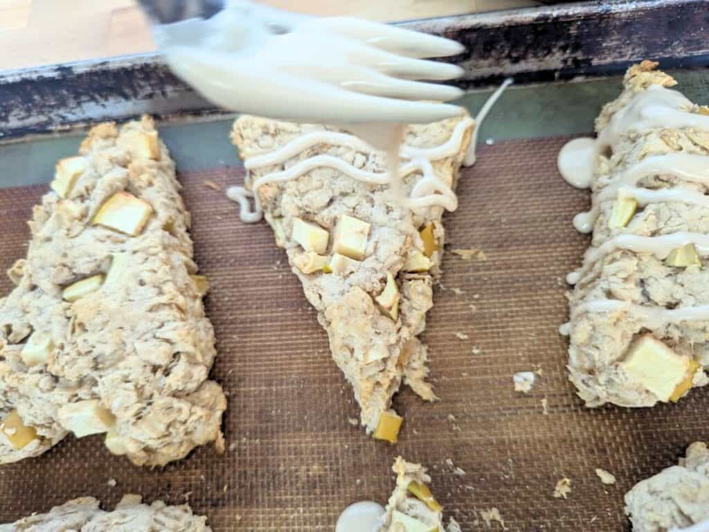 Image shows a fork Drizzling glaze over an apple scone with a fork.