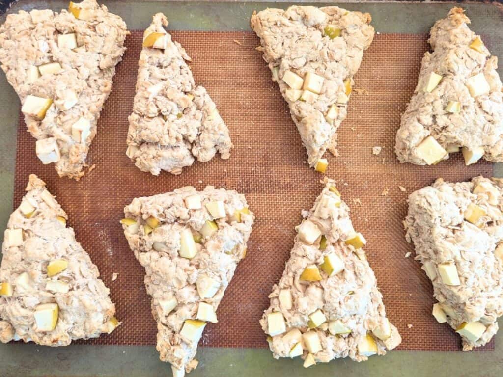 Image shows Eight unbaked apple scone dough pieces arranged on a Silpat.