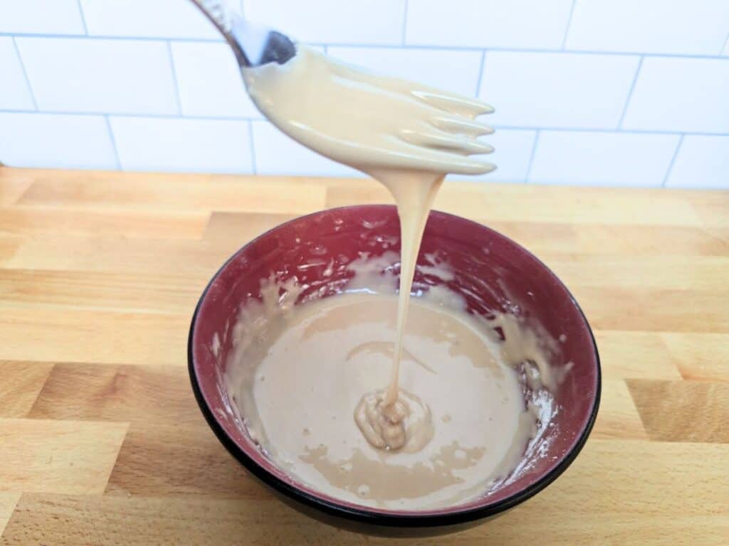 Image shows Sweet glaze for apple scones mixed in a bowl with a fork drizzling it into the bowl.