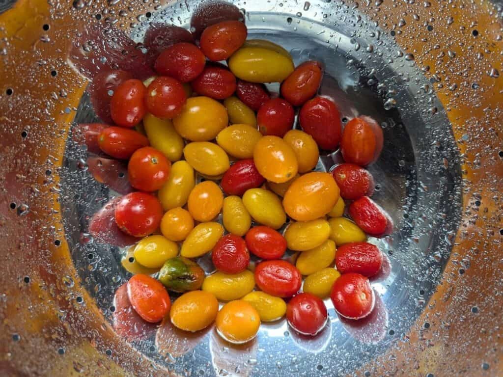 Image shows A bowl of freshly washed tomatoes with water droplets on the skin.