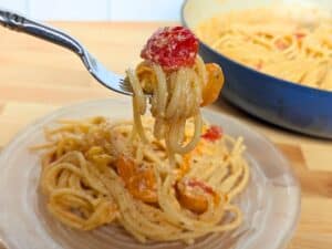Image shows a fork with pasta twirled around it in a light creamy sauce with fresh tomatoes.