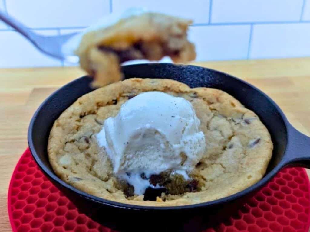 Image shows a spoonful of cookie in the foreground is blurred, with a clear view of the individual chocolate chip skillet cookie in the background.