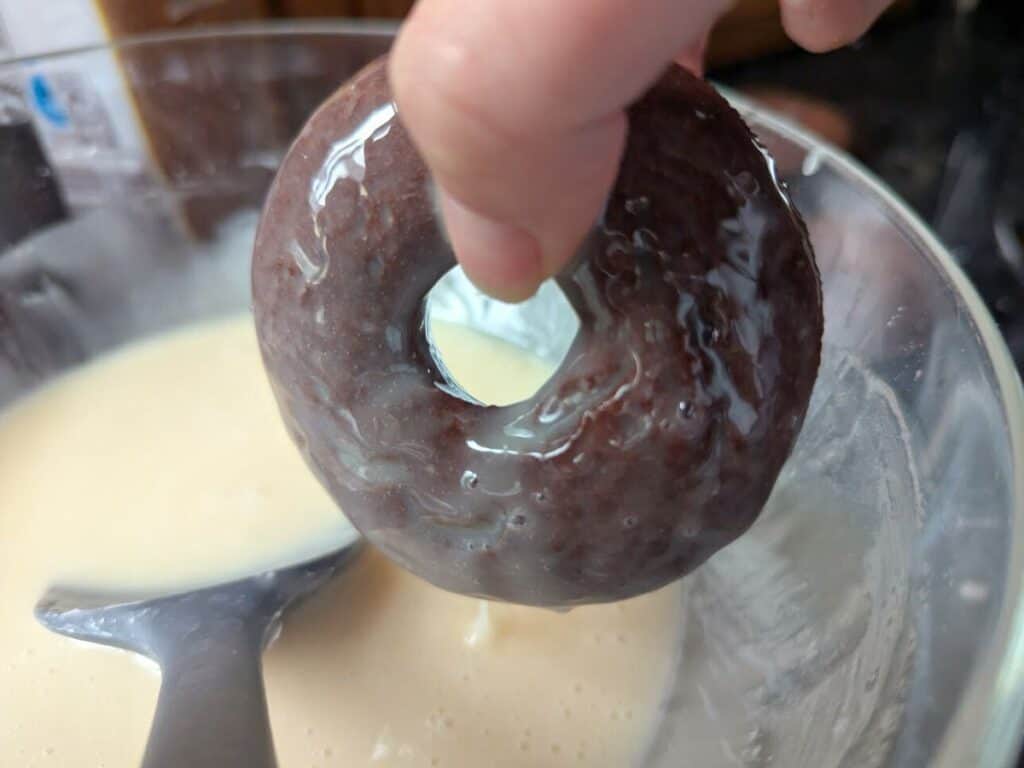 Image shows Adding glaze to freshly baked chocolate donuts.