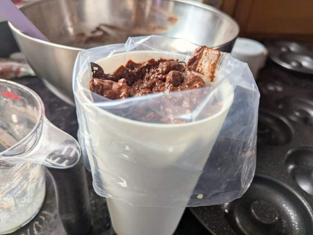 Image shows Chocolate donut batter in a piping bag, ready for filling pans.