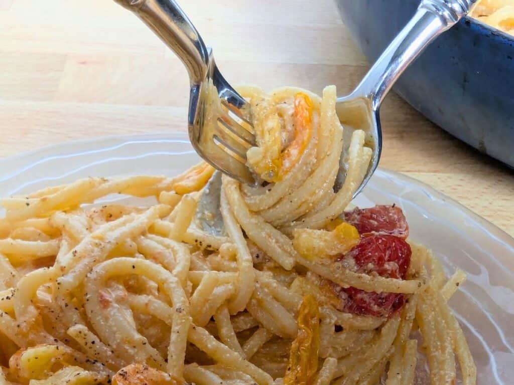 Image shows a fork and spoon twirling homemade pasta with tomatoes.