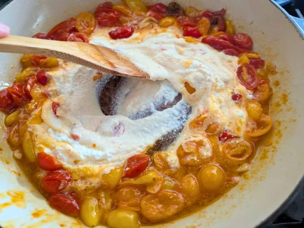 Image shows ricotta cheese being stirred into tomatoes to make a creamy sauce.