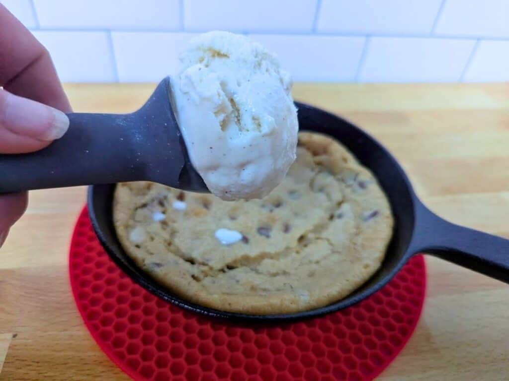 Image shows hand holding a scoop of ice cream over an individual chocolate chip skillet cookie.