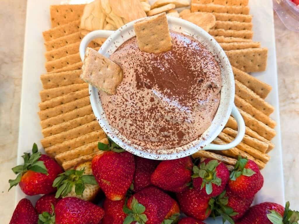 Image shows overview of hot chocolate dip with two crackers dipped in it, and crackers and strawberries on the side.