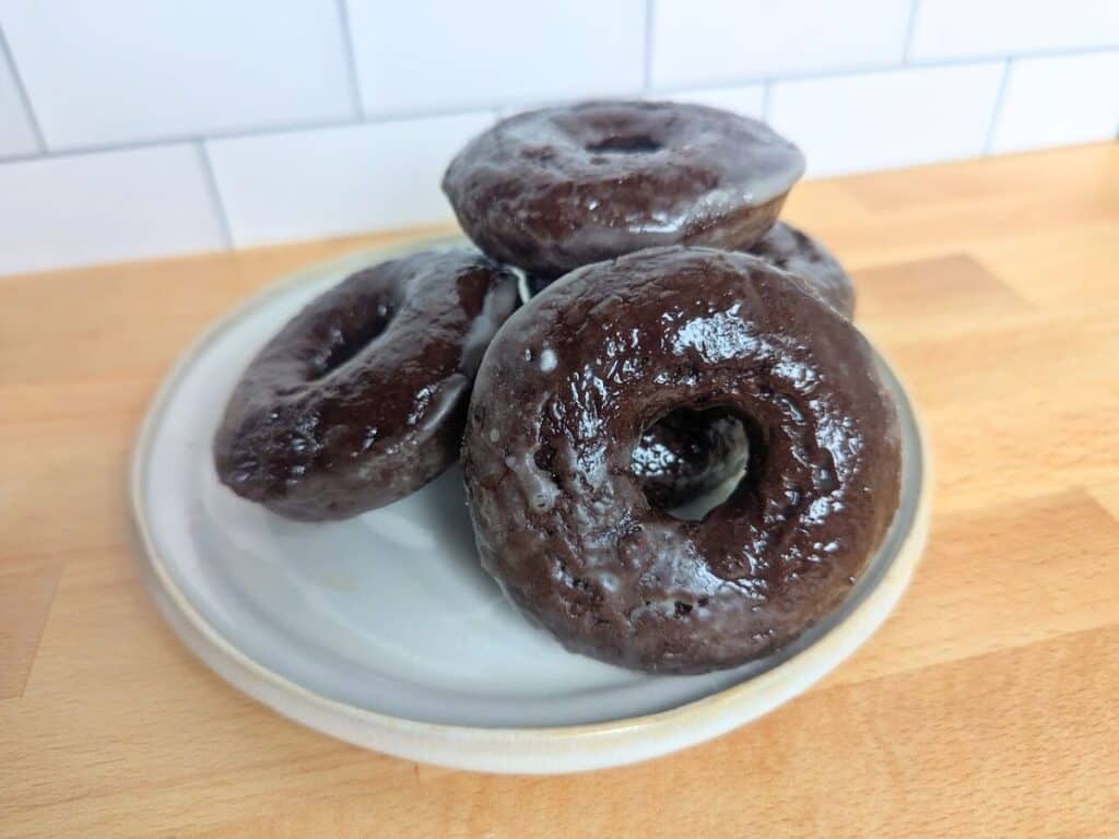 Image shows a Plate of glazed chocolate donuts ready to be served.