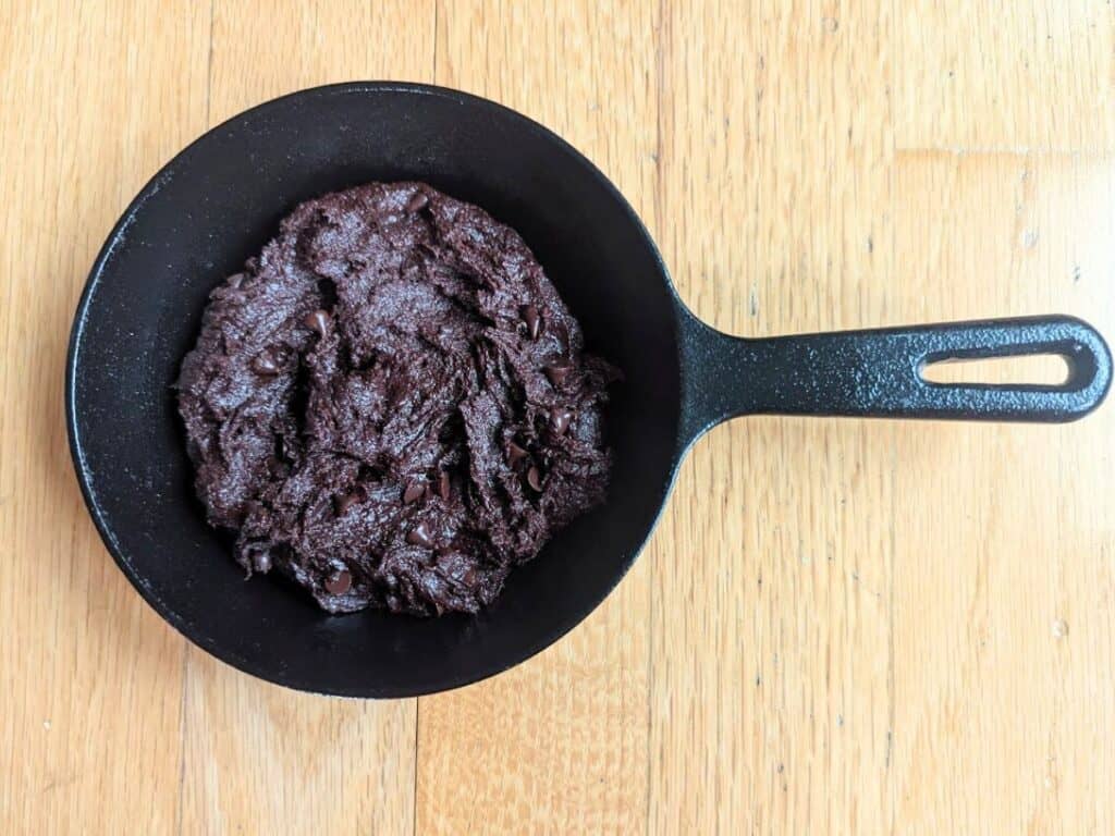 Image shows brownie batter spread in a skillet before baking.