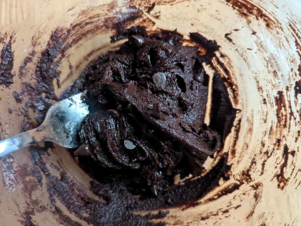 Image shows flour, cocoa powder, salt, and chocolate chips mixed into the wet ingredients for an espresso brownie cookie.