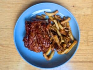 Image shows overhead view of a slice of baby back ribs served with fries on the side..