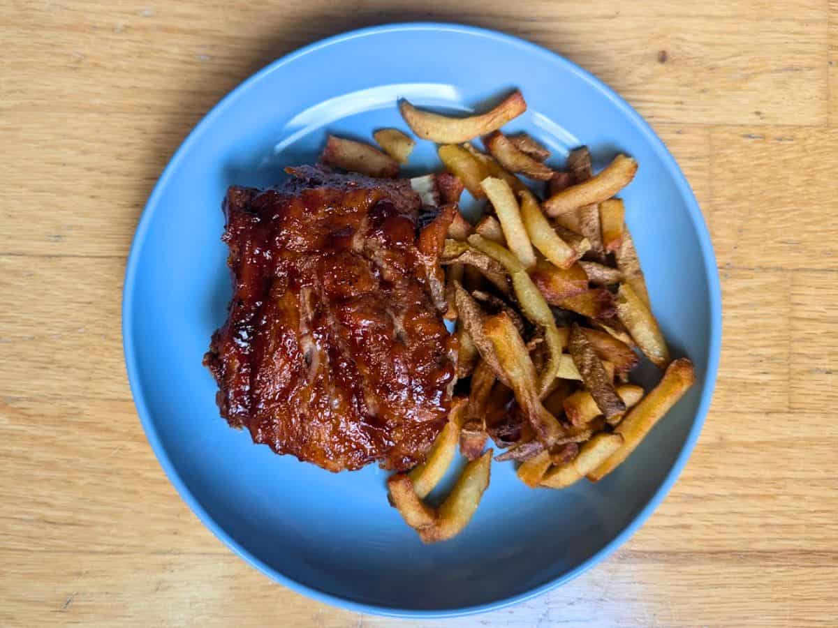 Image shows overhead view of a slice of baby back ribs served with fries on the side..