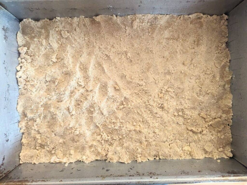 Image shows shortbread base pressed into a 13 by 9 inch pan.