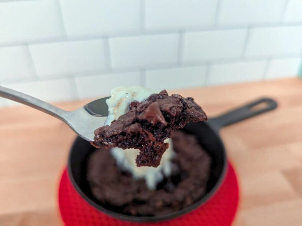 Image shows spoonful of brownie skillet cookie.